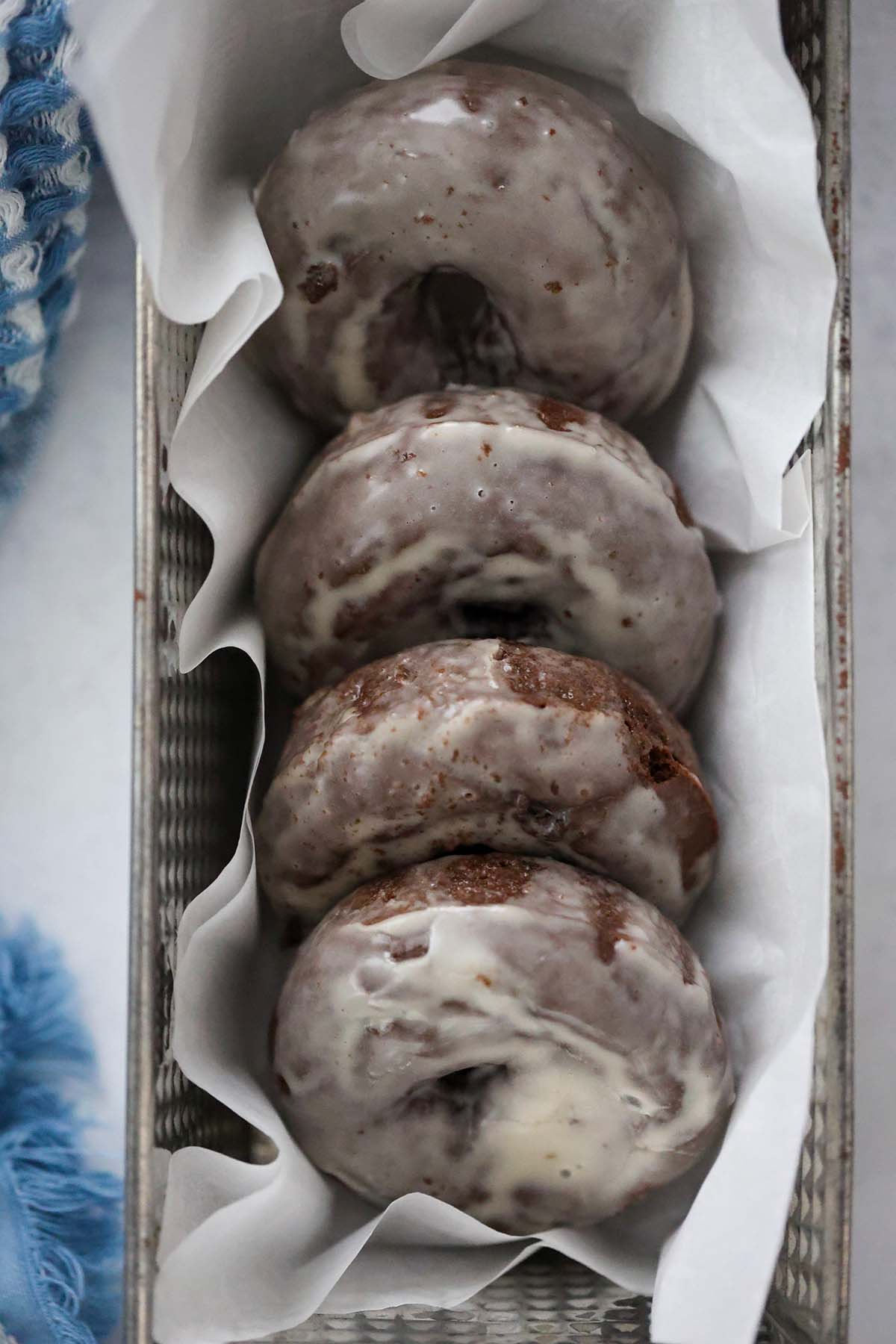 Four chocolate glazed donuts in a loaf pan with parchment paper. 