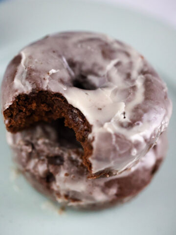 two chocolate glazed donuts on a plate.