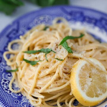 creamy lemon spaghetti on a blue plate with a lemon slice on the side.