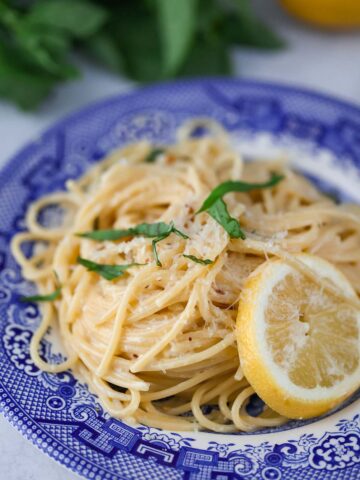 creamy lemon spaghetti on a blue plate with a lemon slice on the side.