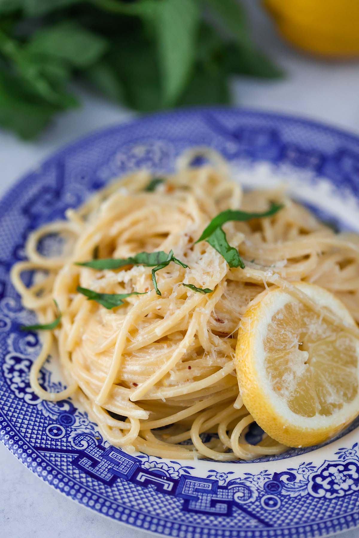 creamy lemon spaghetti on a blue plate with a lemon slice on the side. 