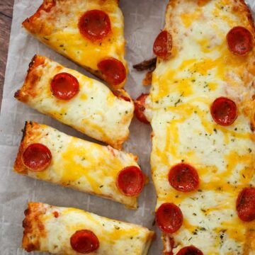 Two French bread pizza loaves with marinara sauce on the side.