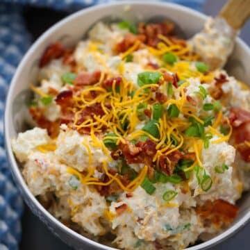 loaded baked potato salad in a bowl with a wooden spoon.