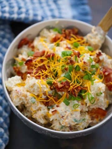 loaded baked potato salad in a bowl with a wooden spoon.