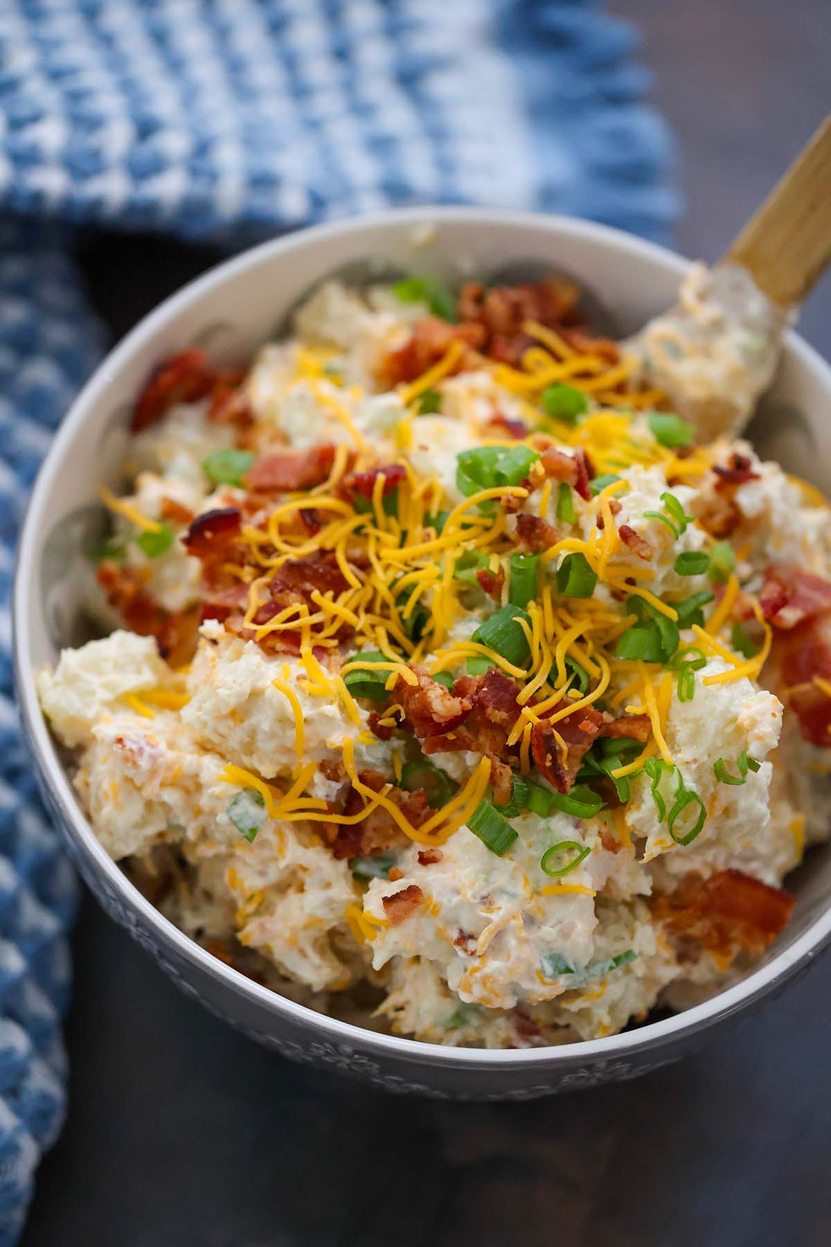 loaded baked potato salad in a bowl with a wooden spoon. 