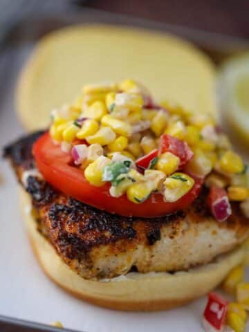 mahi mahi sandwich with corn salad on top.