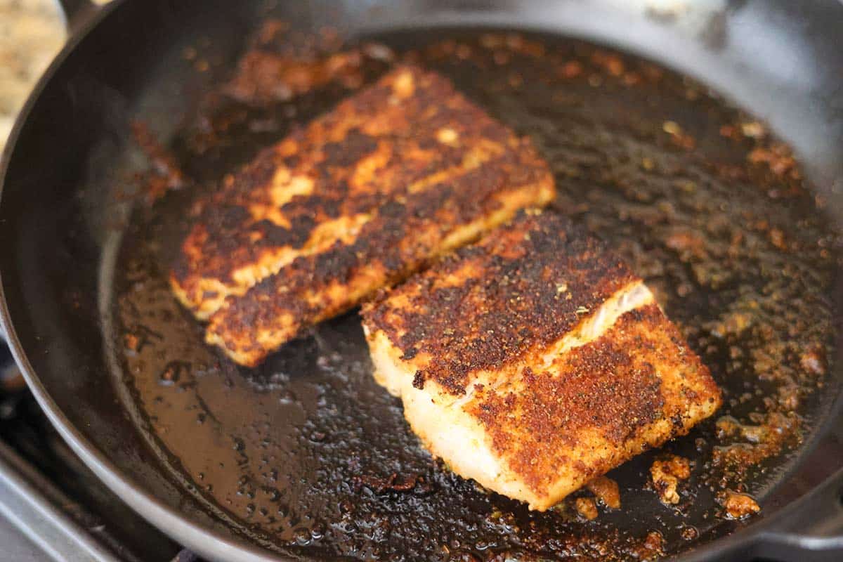two mahi mahi fillets cooking in a skillet on the stovetop. 
