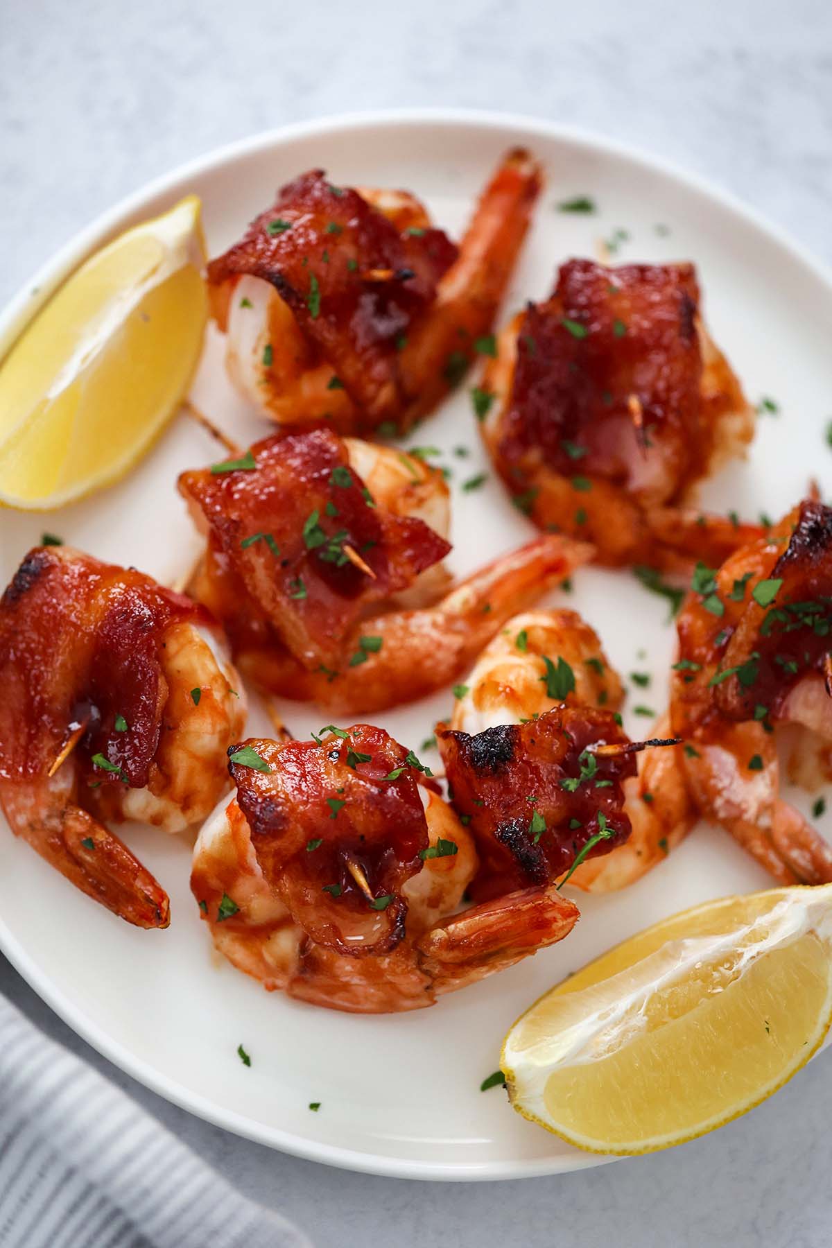 bacon wrapped shrimp on a white plate with lemon wedges on the side. 