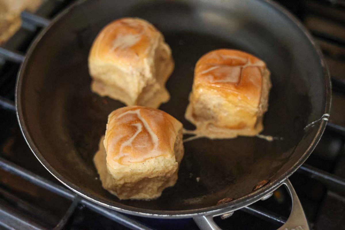 Three Hawaiian rolls cooking in a skillet on the stovetop. 
