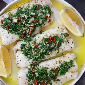 Three cod fillets with chimichurri on top and lemon wedges on the side.