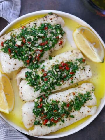 Three cod fillets with chimichurri on top and lemon wedges on the side.