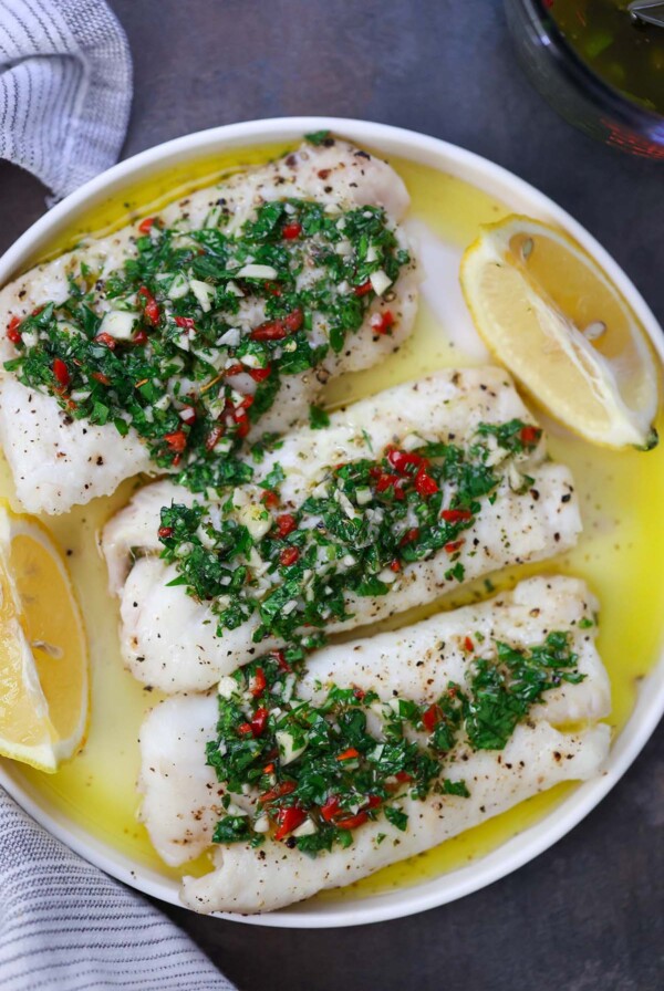Three cod fillets with chimichurri on top and lemon wedges on the side.