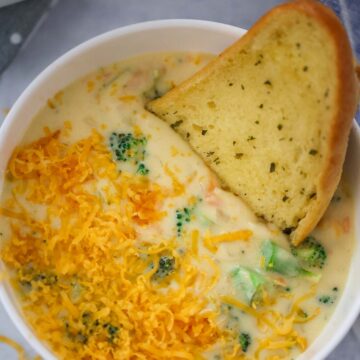 broccoli cheese soup in a white bowl with a piece of bread on the side.