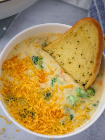 broccoli cheese soup in a white bowl with a piece of bread on the side.