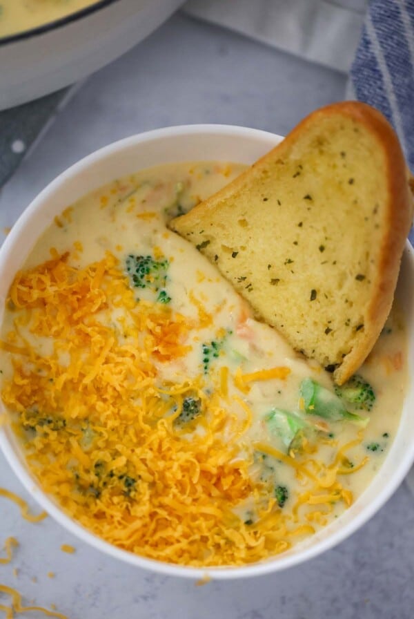 broccoli cheese soup in a white bowl with a piece of bread on the side.