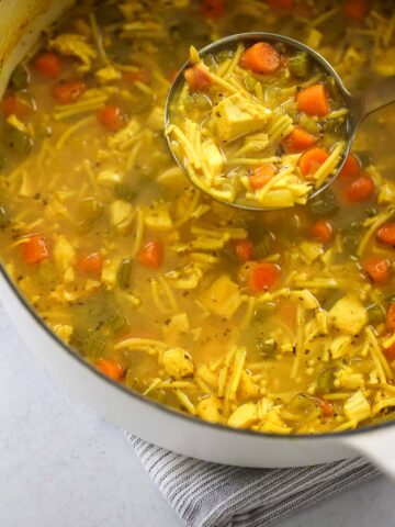 chicken noodle soup in a dutch oven with a ladle.