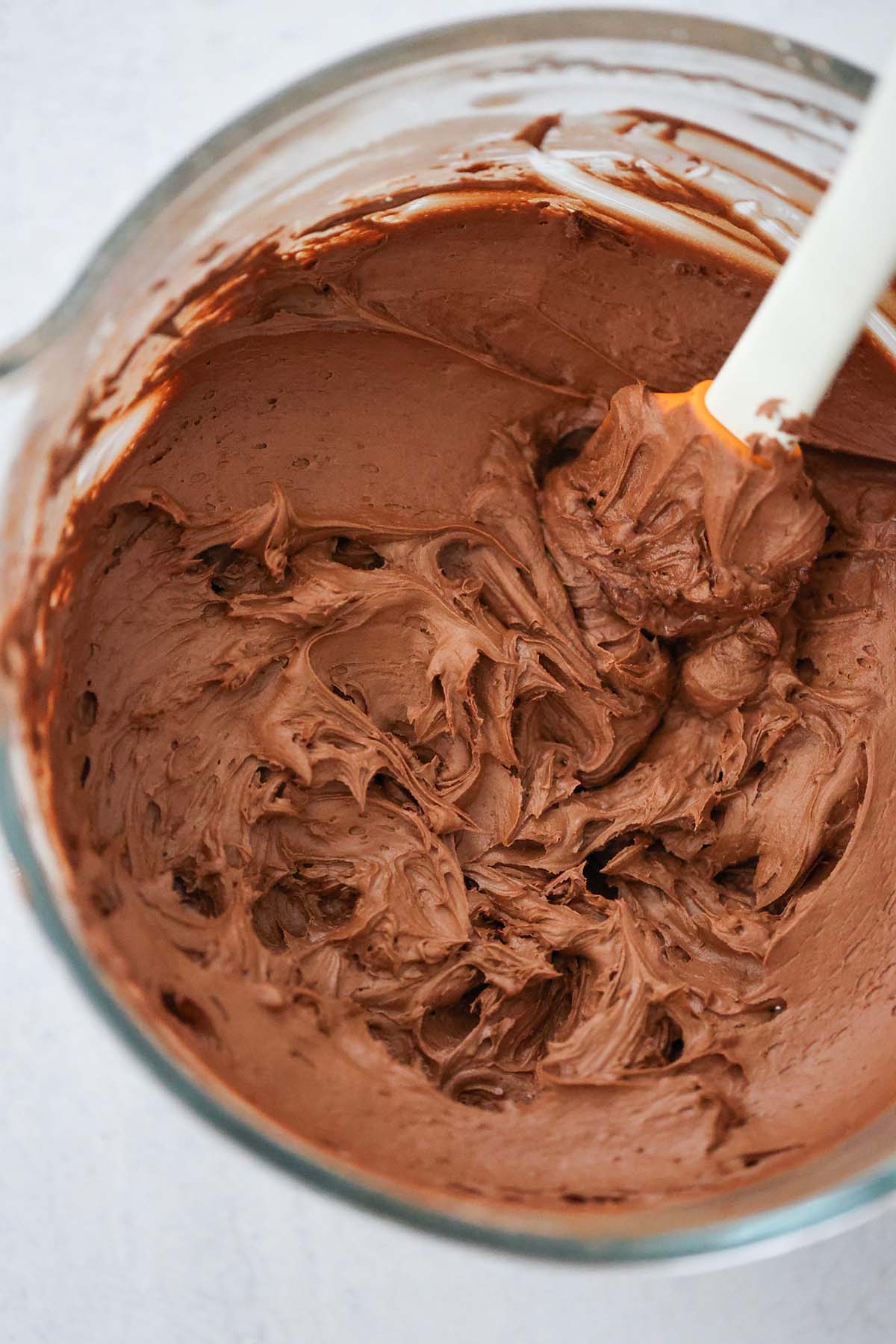 chocolate cream cheese frosting in a glass bowl with a rubber spatula.