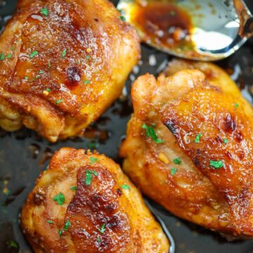 Three honey garlic chicken thighs in a skillet with a spoon.