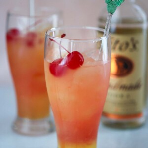 two sex on the beach drinks with a bottle of vodka in the background.