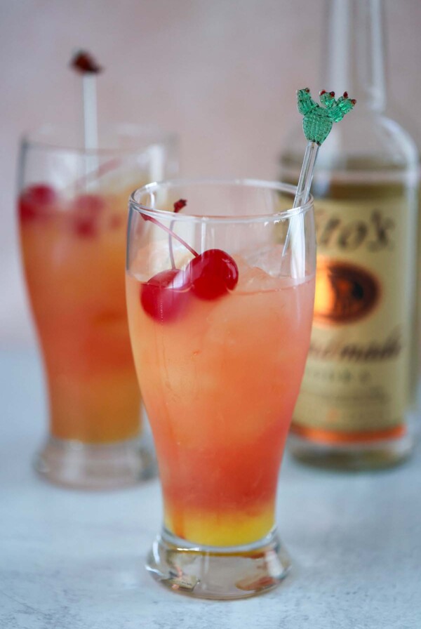 two sex on the beach drinks with a bottle of vodka in the background.