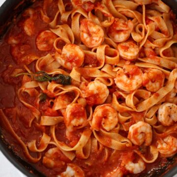 shrimp arrabbiata with tagliatelle in a black skillet.