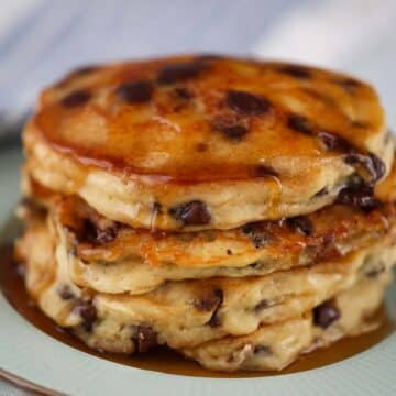 four chocolate chip pancakes with maple syrup on a plate.