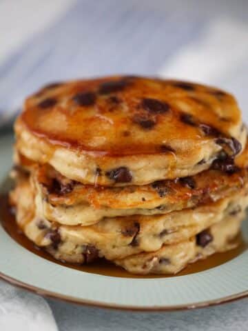 four chocolate chip pancakes with maple syrup on a plate.