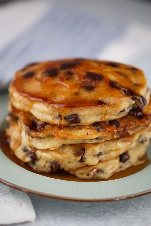 four chocolate chip pancakes with maple syrup on a plate.