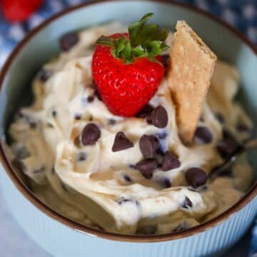 chocolate chip cheesecake dip in a bowl with a strawberry and graham cookie on top.