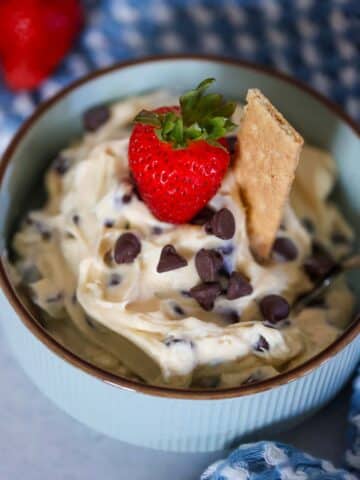 chocolate chip cheesecake dip in a bowl with a strawberry and graham cookie on top.