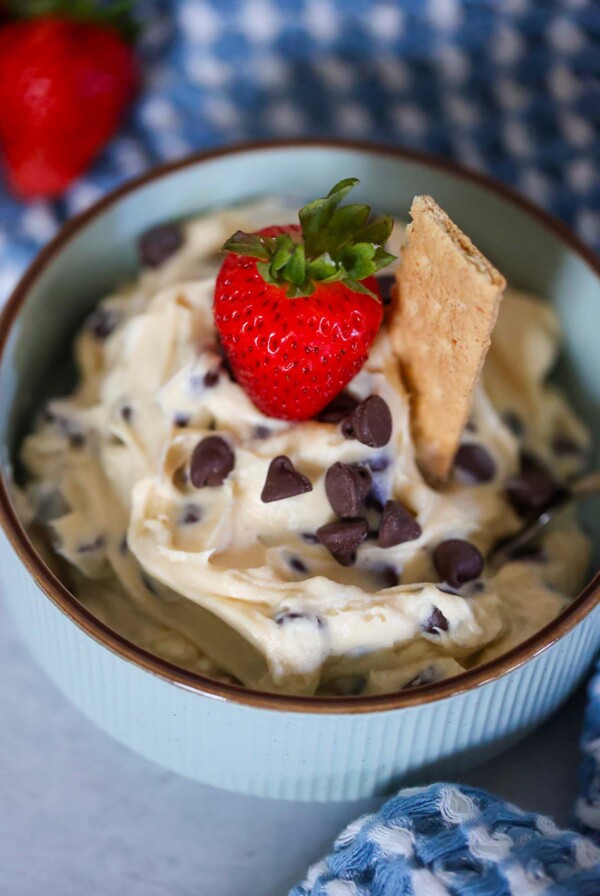 chocolate chip cheesecake dip in a bowl with a strawberry and graham cookie on top.