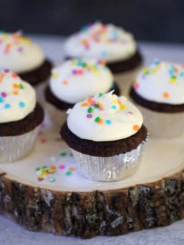 Six chocolate cupcakes with cream cheese frosting and sprinkles.