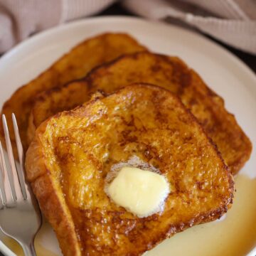 pumpkin french toast with butter and maple syrup on a white plate.