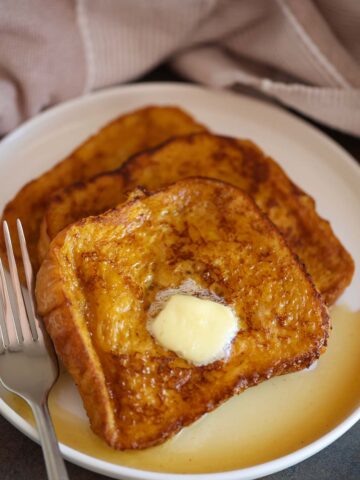 pumpkin french toast with butter and maple syrup on a white plate.