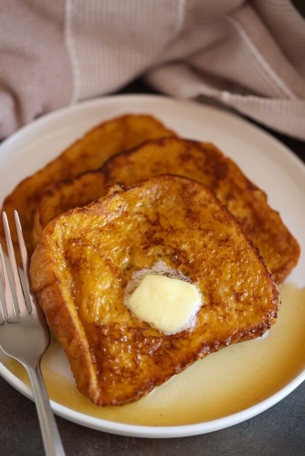pumpkin french toast with butter and maple syrup on a white plate.