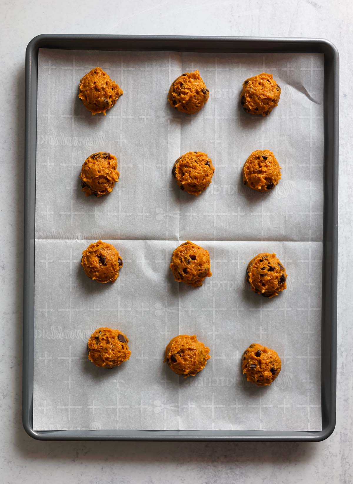twelve cookie dough balls on a baking sheet. 