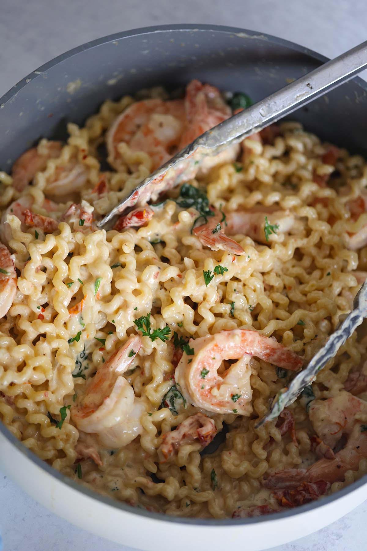 Pasta and shrimp in a skillet with tongs. 
