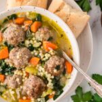 Italian wedding soup in a bowl with a spoon and bread on the side.