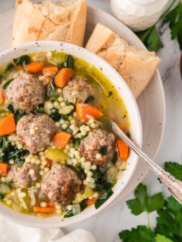 Italian wedding soup in a bowl with a spoon and bread on the side.