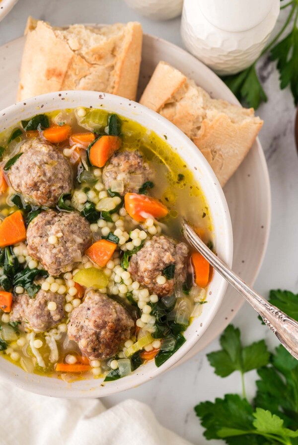 Italian wedding soup in a bowl with a spoon and bread on the side.