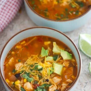 two bowls of chicken noodle taco soup with a lime wedge on the side.