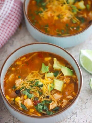 two bowls of chicken noodle taco soup with a lime wedge on the side.