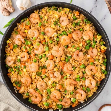 shrimp fried rice in a large skillet with onions and ginger on the side.