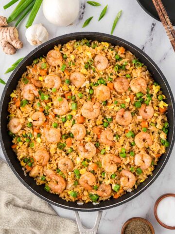 shrimp fried rice in a large skillet with onions and ginger on the side.