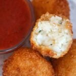 Three cheese arancini with marinara sauce on the side.