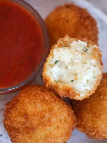 Three cheese arancini with marinara sauce on the side.