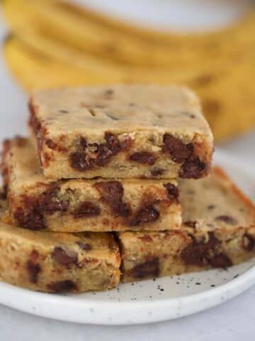 chocolate banana bars on a plate with ripe bananas in the background.