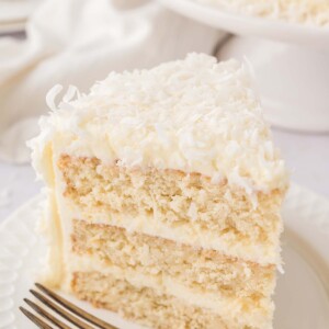 A slice of coconut cake on a white plate with a fork.