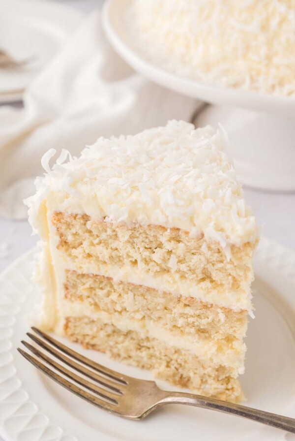 A slice of coconut cake on a white plate with a fork.