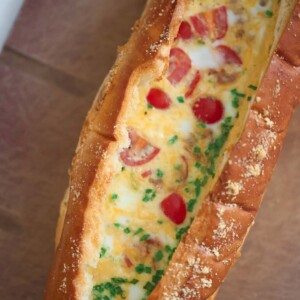 baked eggs with tomatoes, chives, and cheese inside of a loaf of bread.